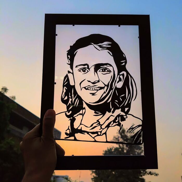 Hand holding intricate paper art portrait of a smiling girl with colorful sunset background showing details of paper art.