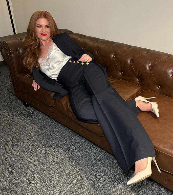 Isla Fisher reclining on a brown leather couch, wearing a black suit and white heels amid divorce tension headlines. Isla Fisher reclining on a brown leather couch, wearing a black suit and white heels amid divorce tension headlines.