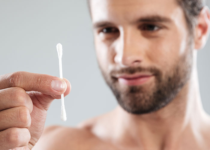 Man holding a cotton swab closely, illustrating one of the things everyone does but doesn’t talk about.