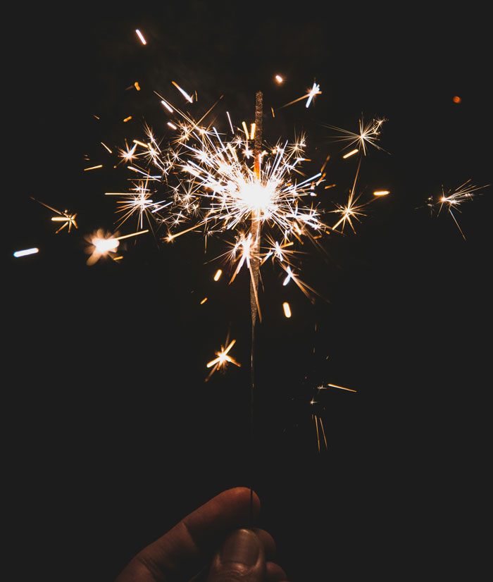 Hand holding a lit sparkler against a dark background illustrating weird parenting rules recalled later.