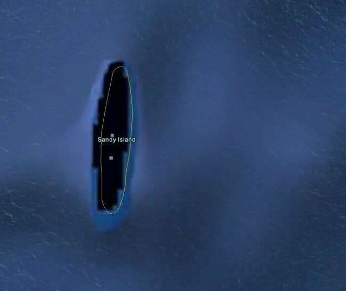 Aerial view of a narrow black island named Sandy Island surrounded by deep blue ocean on Google Earth.