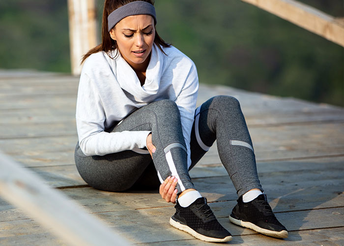 Woman sitting outdoors holding her ankle in pain, illustrating the most pathetic injuries people have experienced.
