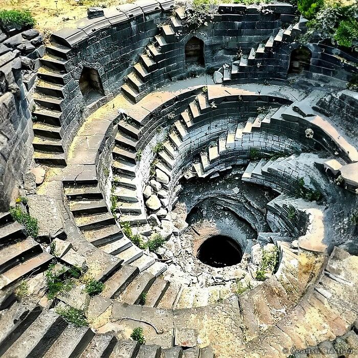 Ancient history stone stepwell with intricate circular staircases and weathered architecture surrounded by vegetation.