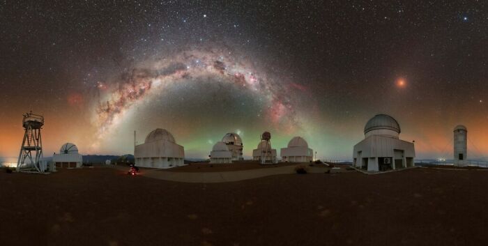 Panoramic view of observatory domes under a vivid Milky Way arch showcasing the beauty of the night sky.