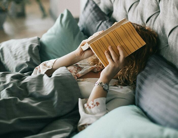 Person lying on couch with a book covering their face, illustrating jobs that shouldn’t be earning as much as they do.