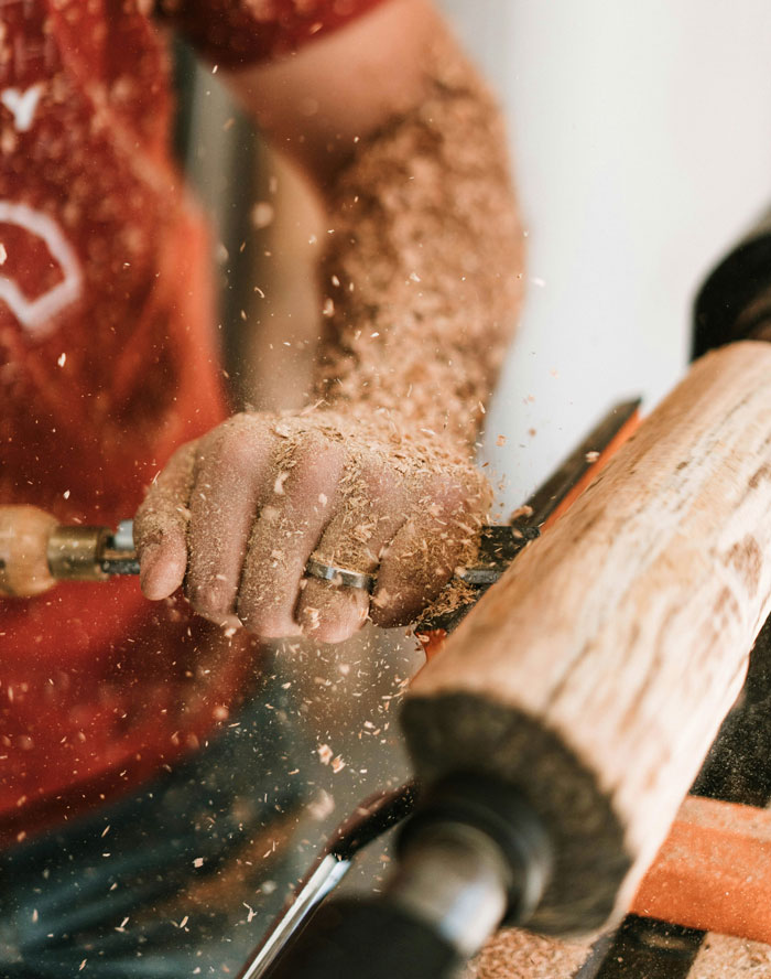 Close-up of woodworking with hand shaping wood and wood shavings flying, illustrating ways people lose money while saving.