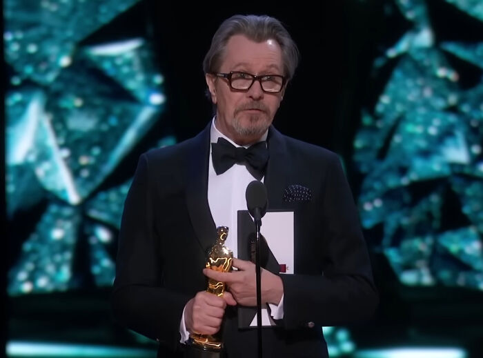 Actor in a tuxedo holding an award and speaking at a microphone, related to miscast actors in movies discussion.
