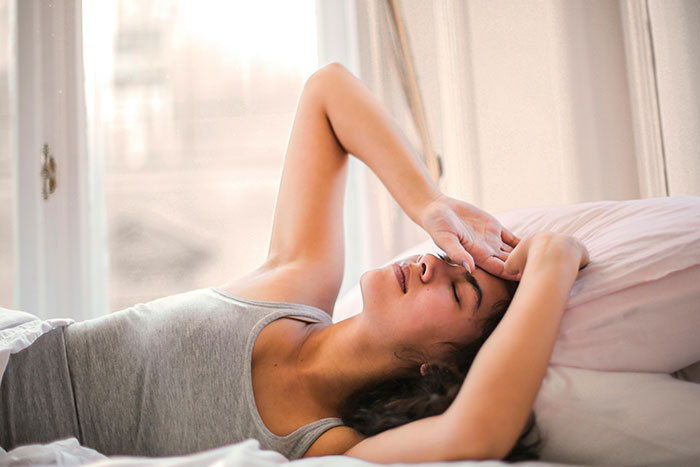 Young woman lying in bed with eyes closed, holding forehead, showing a scary gut feeling to leave now moment.
