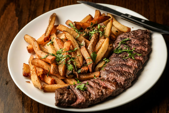 Steak and fries garnished with herbs on a white plate, illustrating unusual family food rules and habits.