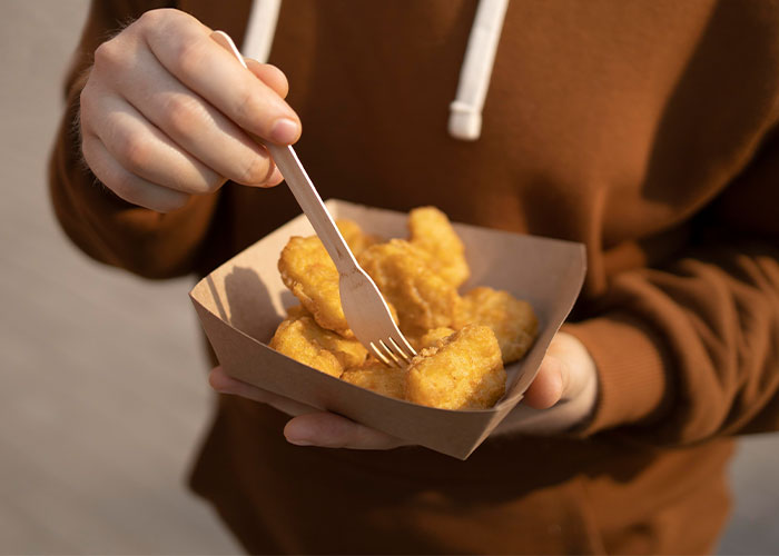 Person in brown hoodie holding a tray of chicken nuggets and picking one with a wooden fork, representing pathetic injuries.