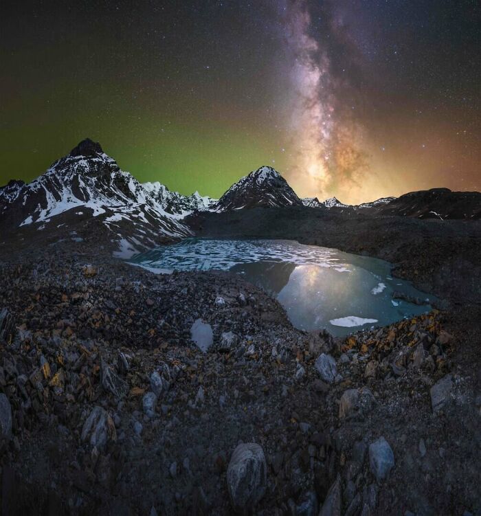 Milky Way shining brightly above snow-capped mountains and a reflective lake under the clear night sky.