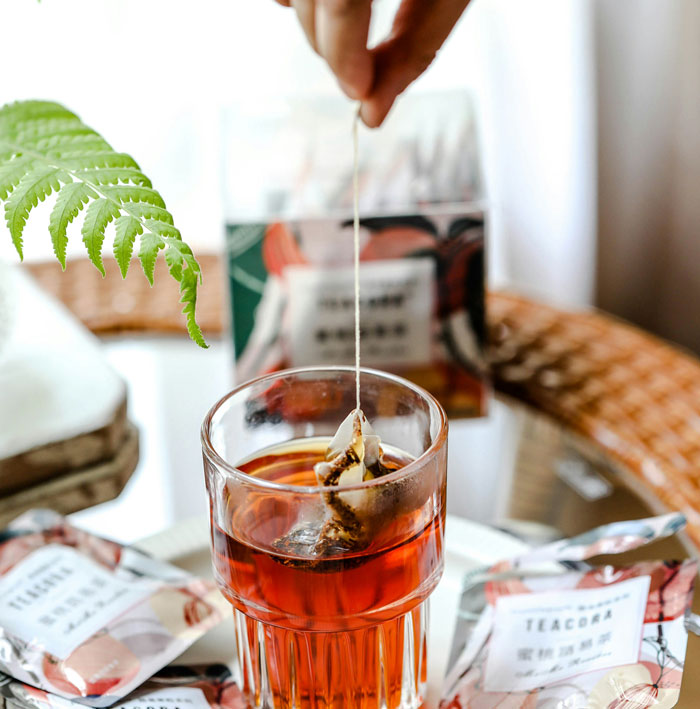 Hand dipping tea bag into glass of tea surrounded by tea packets illustrating weird habits from being raised poor