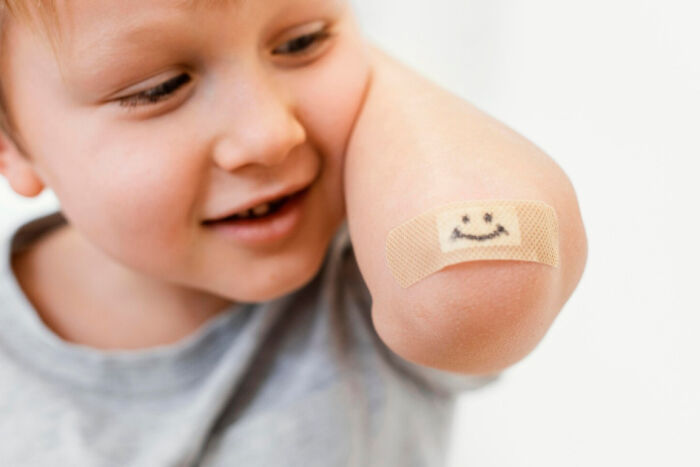 Young child smiling and showing elbow with adhesive bandage featuring a drawn smiley face illustrating placebo effect in real life.