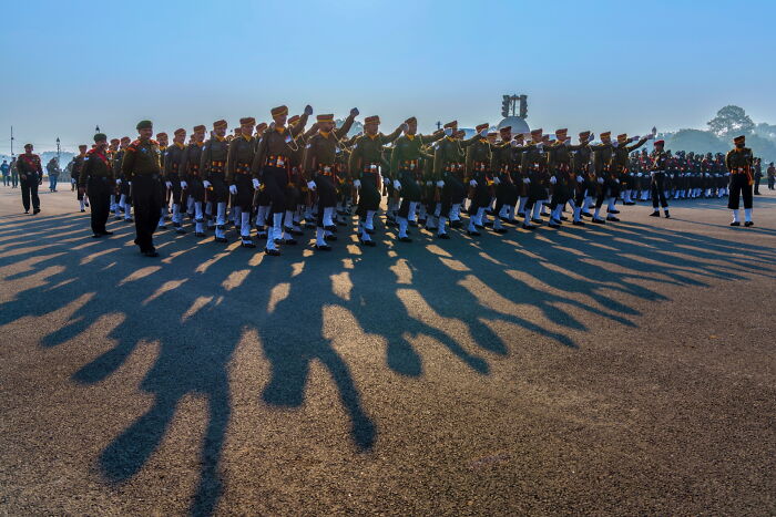 Soldiers marching in formation during a ceremony captured in pure street photography style with long shadows on the ground.