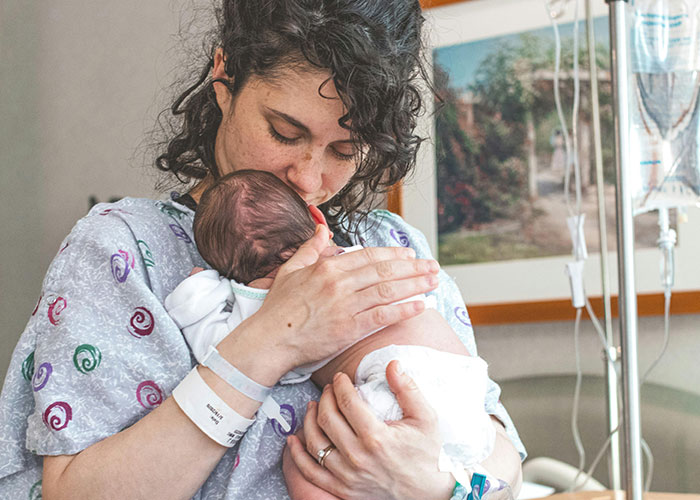 Mother in hospital gown holding newborn baby close, capturing a tender moment related to entertaining facts shared on X.