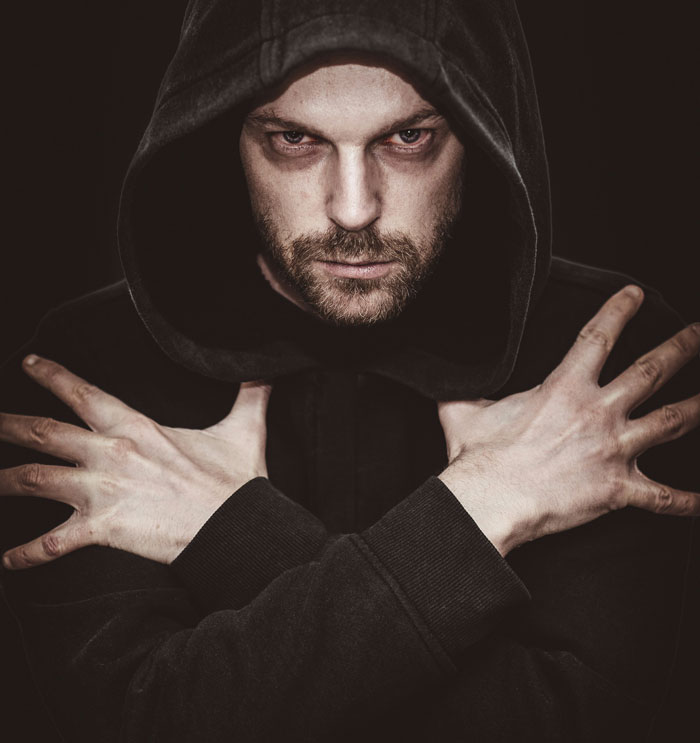 Man in black hoodie crossing arms with intense gaze, symbolizing people who escaped from cults sharing their experiences.