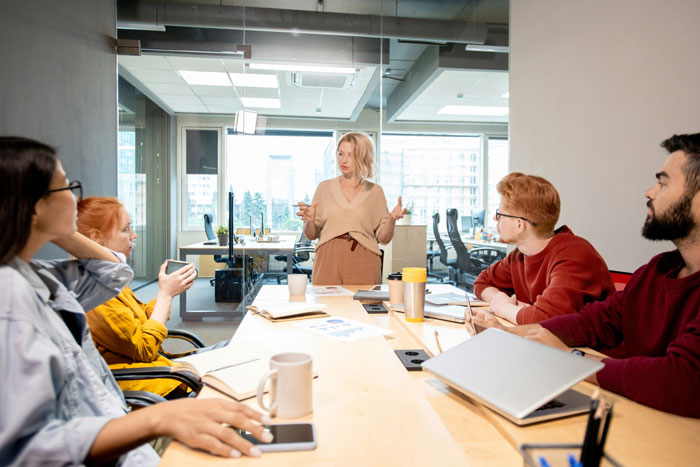 Team meeting with a woman leading a discussion while others listen, illustrating infuriating things said by people in charge.