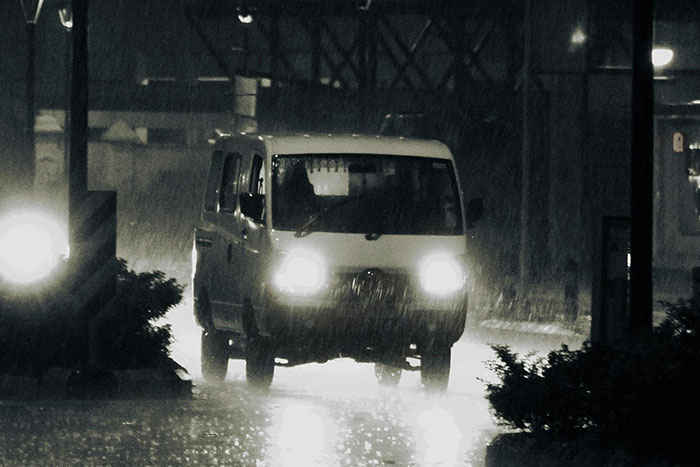 White van with headlights on driving through heavy rain and darkness, capturing a scary gut feeling moment to leave now