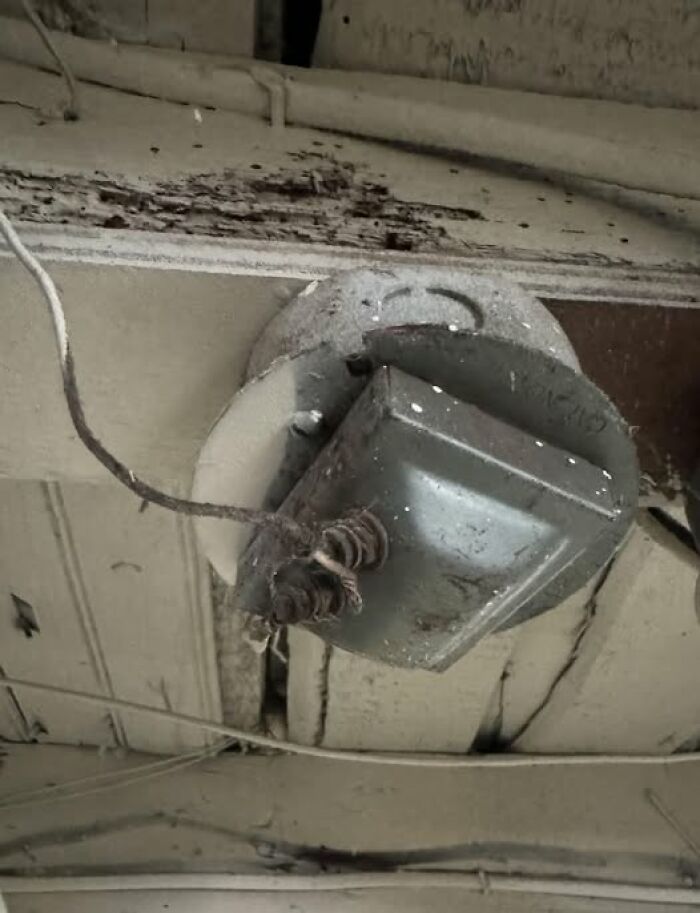 Old rusty electrical fixture with exposed wires mounted on a ceiling in a home with a hidden haunted past.