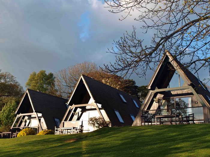 Modern triangular houses on a grassy hill under cloudy sky, illustrating ways people lose money while thinking they’re saving.