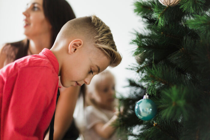 Young boy and children decorating a Christmas tree with ornaments in a cozy home setting during the holiday season.