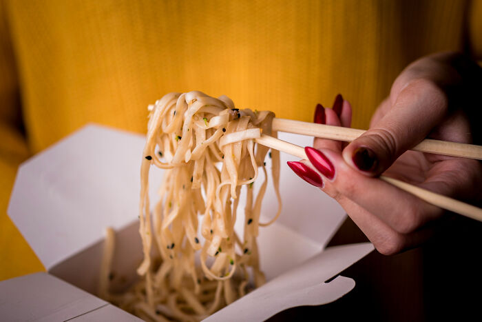 Hand holding chopsticks lifting noodles from takeout box, representing wild cooking opinions and internet food thoughts.