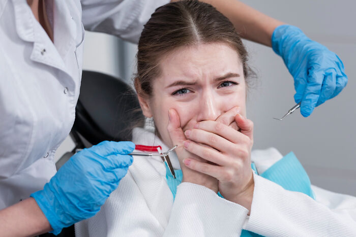 Young woman at dentist looking scared and covering mouth, illustrating casual things that can actually be deadly risks.