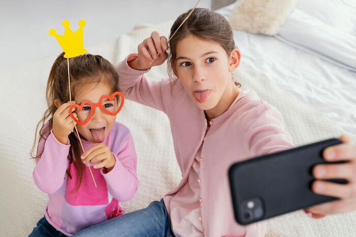 Two girls making funny faces and taking selfies while playing with props, capturing wildest life blunders moments.