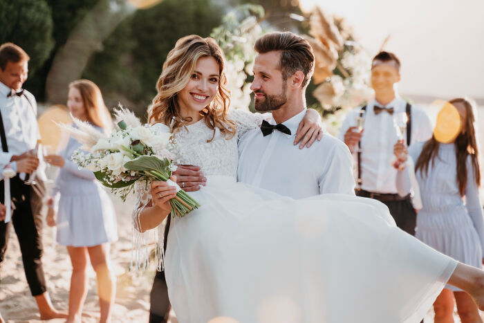 Happy bride being carried by groom at outdoor wedding, capturing moments from an adult life feeling like gym class.