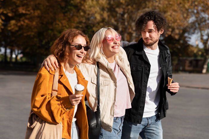 Three young adults laughing and walking together outdoors, capturing moments from an adult life feeling socially awkward.