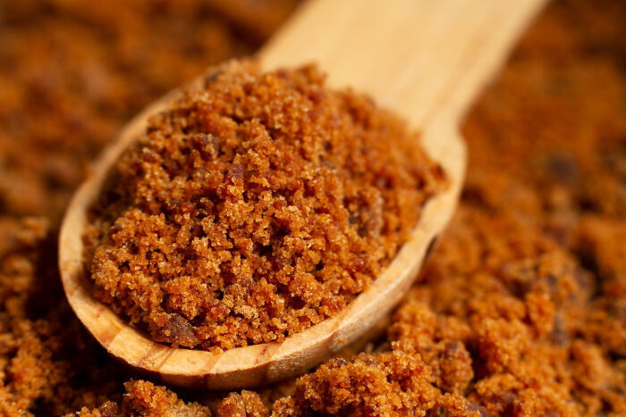 Close-up of a wooden spoon filled with coarse brown sugar, illustrating wild cooking opinions on ingredient choices.