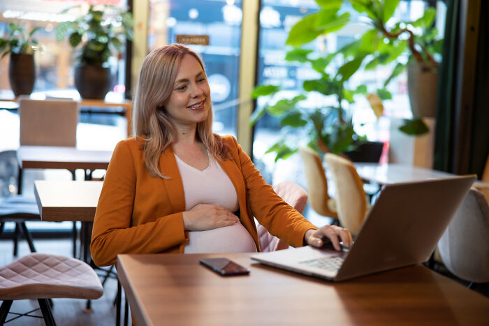 Pregnant woman smiling while using a laptop in a cozy cafe, reflecting on a small decision that changed her life forever.