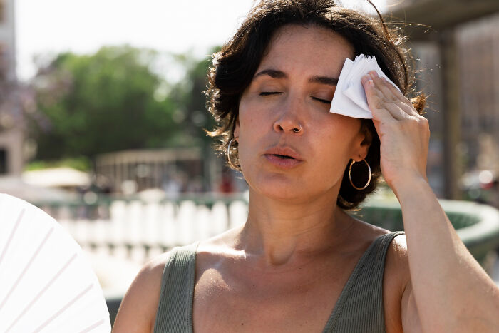 Woman wiping sweat from forehead with tissue outdoors on a hot day, highlighting casual things that can be deadly.