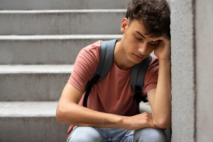 Teenage boy sitting on stairs with backpack, looking sad and distressed reflecting on soul-crushing things parents said.