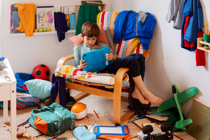 Young boy sitting in a colorful chair surrounded by toys and clothes, illustrating childhood challenges and family dynamics.
