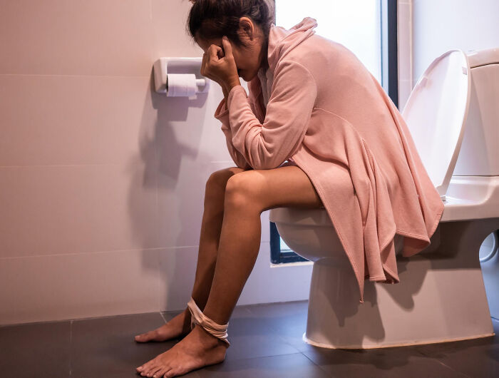 Woman sitting on toilet looking distressed in a bathroom, illustrating a tiny thing that made trip better concept.