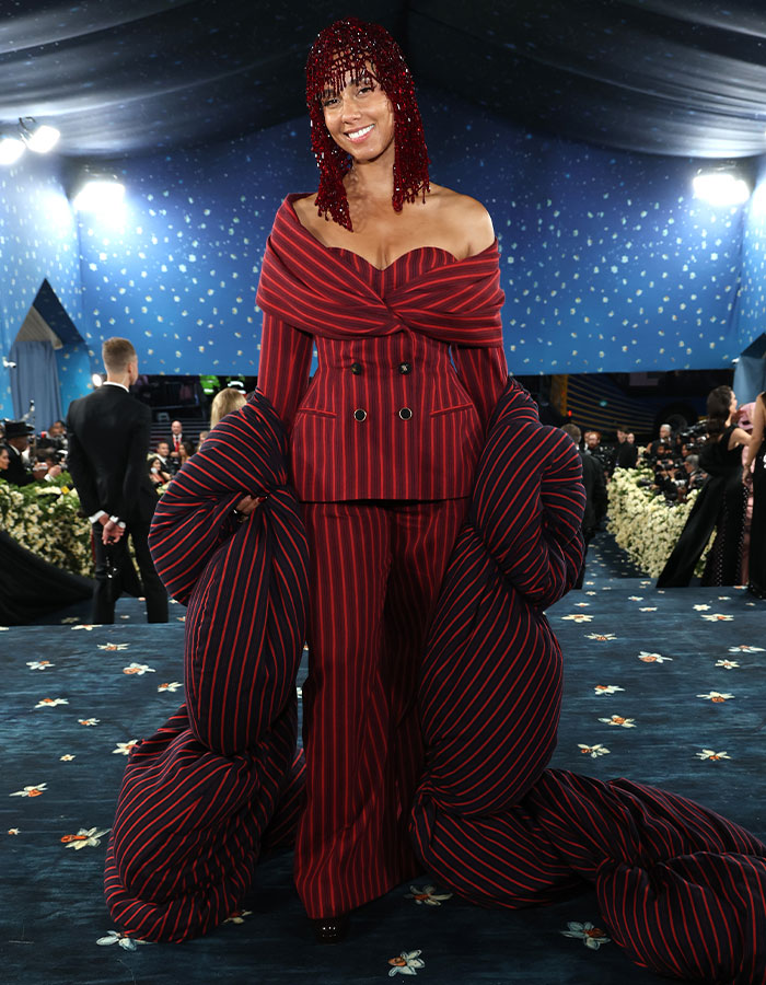 Woman wearing oversized red and black striped suit with dramatic padded sleeves at a 2025 event, showcasing fashion fails.