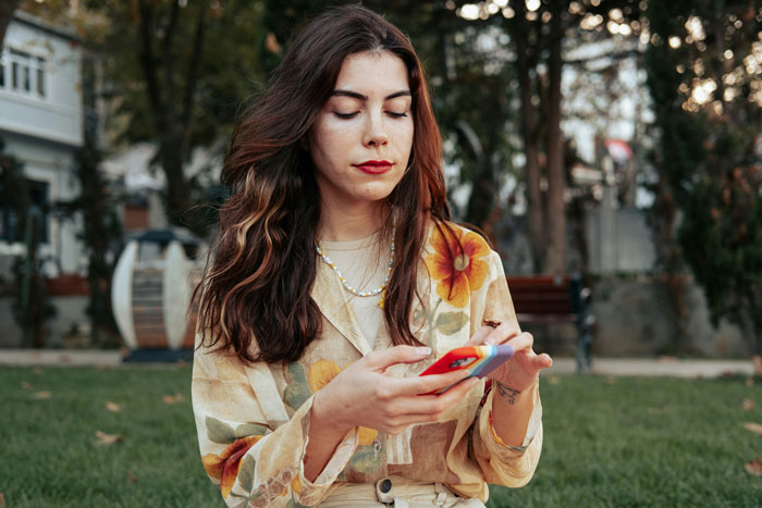 Young woman sitting outdoors using a smartphone, reflecting on friendship of 10+ years ended and lost connections.