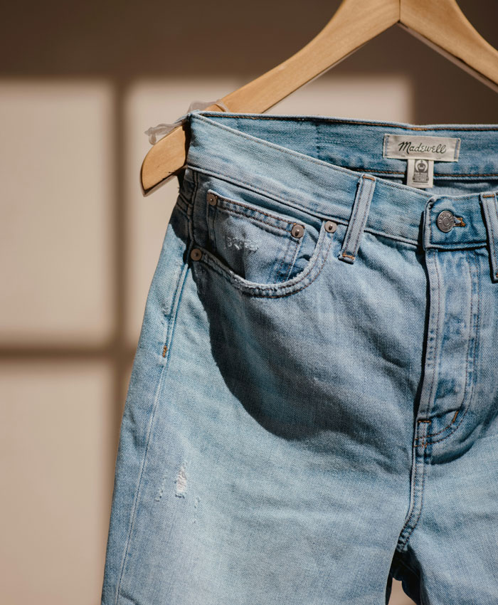 Light blue jeans hanging on a wooden hanger with sunlight and shadows, reflecting one weird parent rule concept.