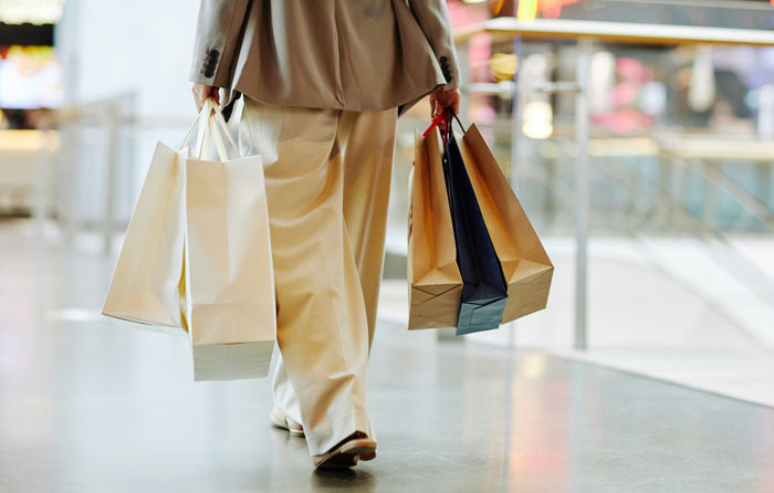 Person walking in a store carrying multiple shopping bags, illustrating common ways people lose money while saving.