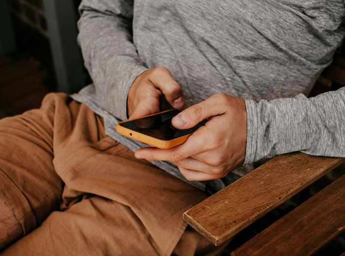 Person wearing casual clothes holding a smartphone, illustrating weird habits that mean I was raised poor.