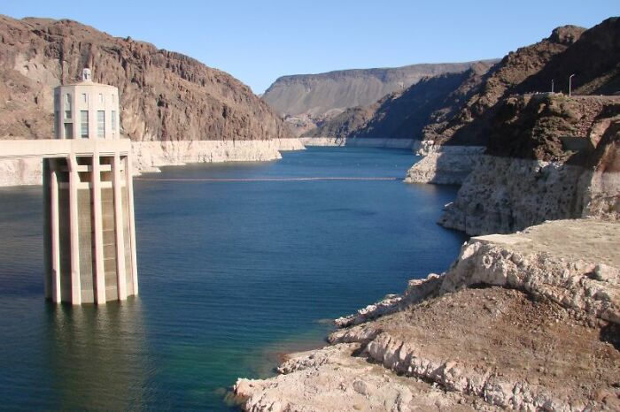 Before and after photo showing dramatic water level changes in a lake surrounded by rocky cliffs and a water intake tower.