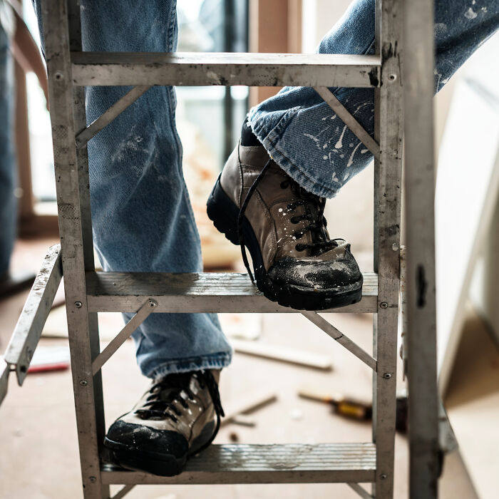 Person wearing sturdy boots climbing a metal ladder, highlighting casual things that can actually be deadly at home.