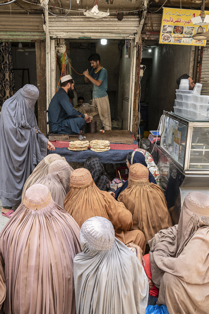 Women in traditional burqas gathered at a market stall with stacks of bread, captured in stunning food photography awards shot.