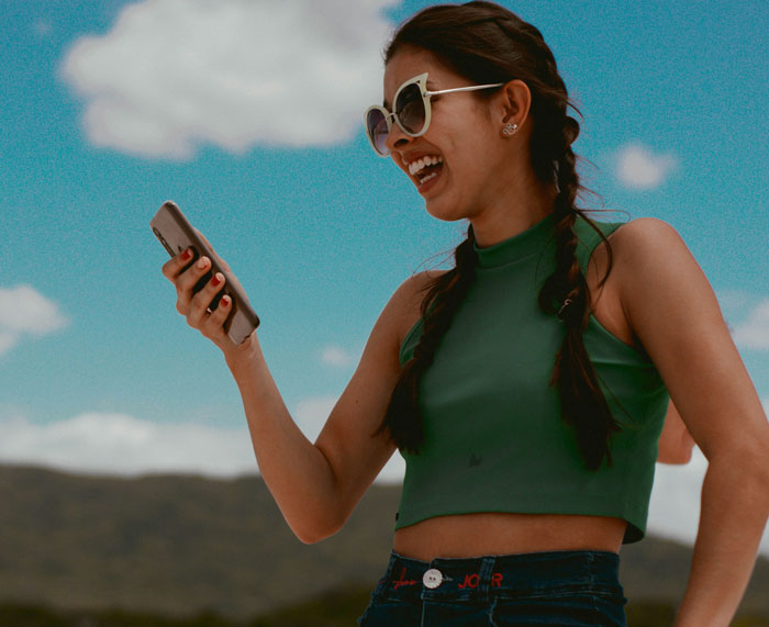 Young woman with braided hair and sunglasses laughing while looking at her phone, illustrating problematic behaviors women get a pass for.