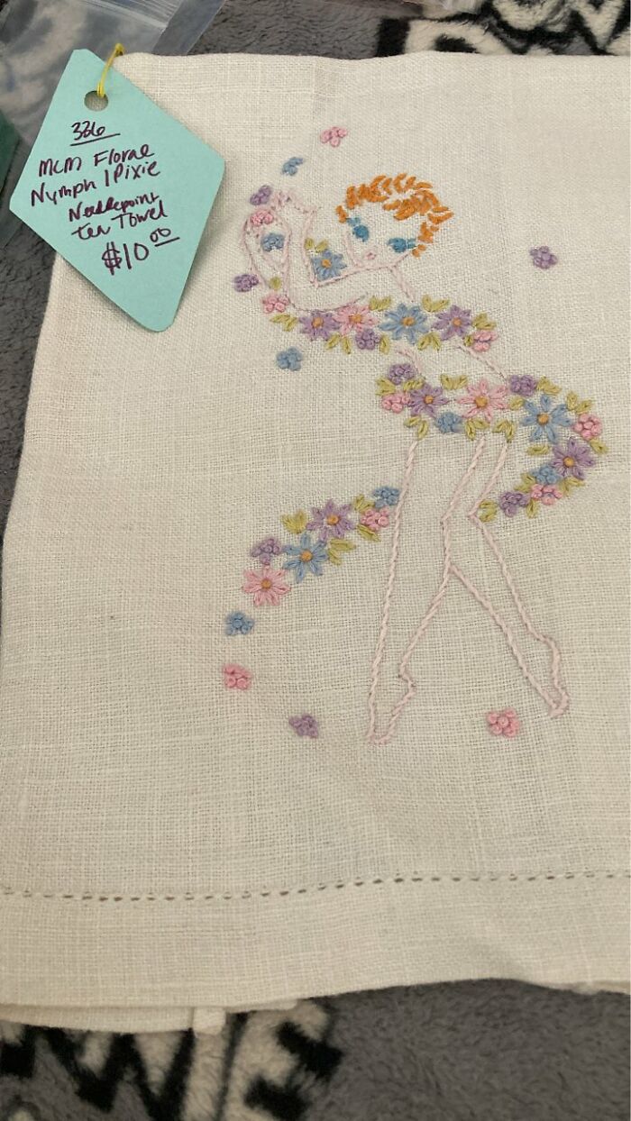 Embroidered vintage tea towel featuring a floral dress figure, a unique thrifted find with museum-worthy charm.
