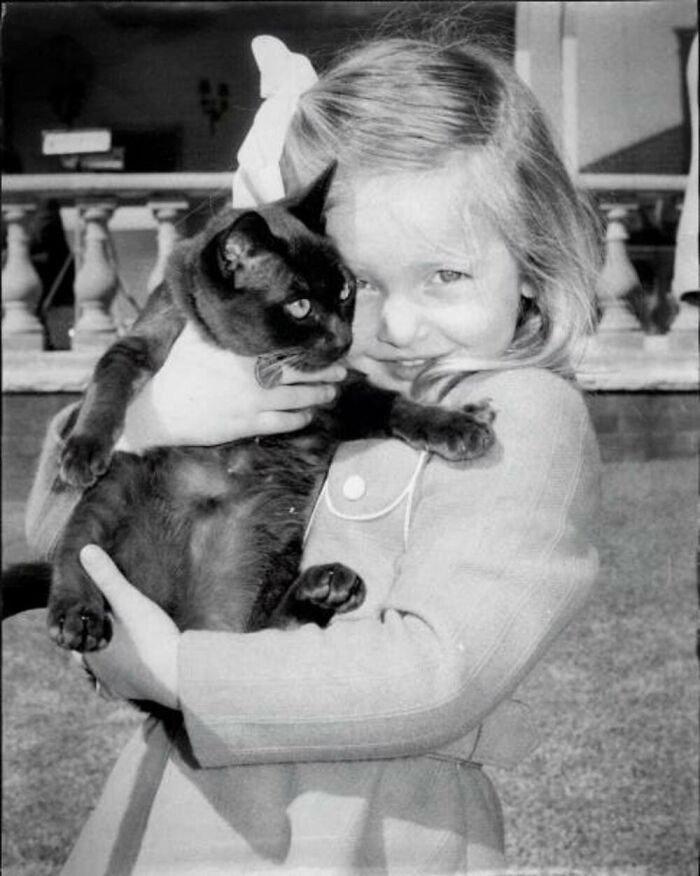 Vintage photo of a young girl lovingly holding a black cat, showcasing the timeless bond between kids and cats.