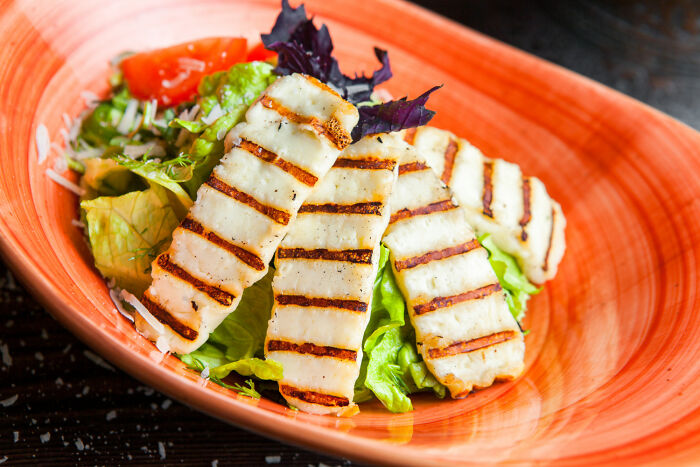 Grilled halloumi cheese slices served on a fresh mixed green salad in an orange bowl.