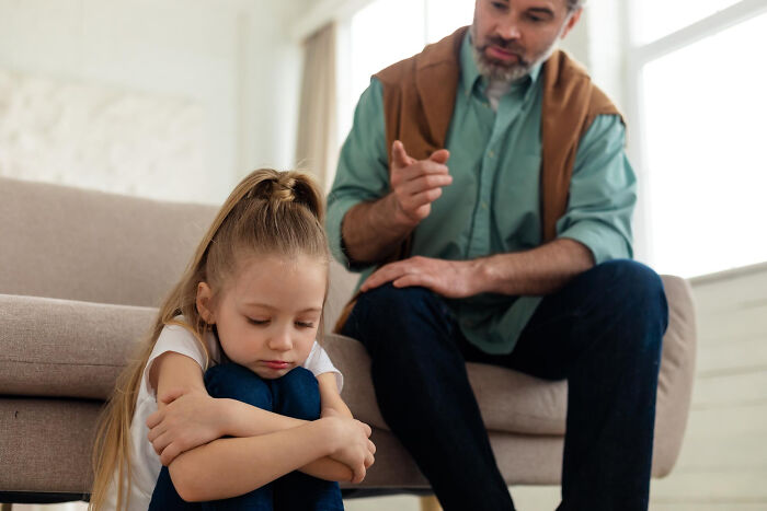 Young girl looking upset while father talks sternly, illustrating soul-crushing things parents told children.