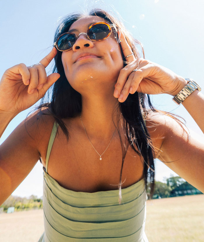 Young woman wearing sunglasses outdoors, smiling and posing confidently, illustrating problematic behaviors women get a pass for.